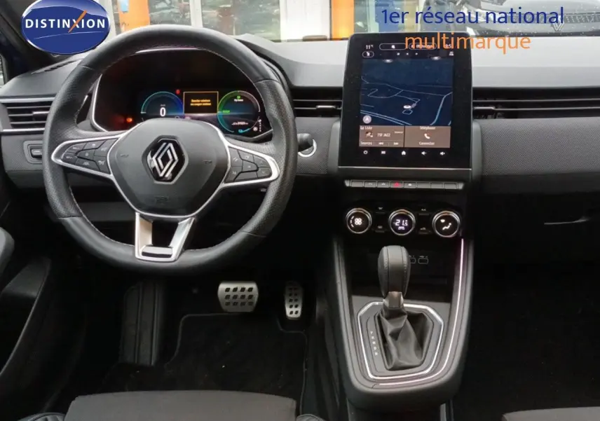 Vue intérieure centrée sur le tableau de bord et volant de la Renault Clio 1.6 E-TECH 2024 avec écran tactile et levier de boîte auto.