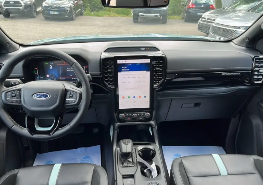 Vue intérieure avant du Ford Ranger Stormtrak 2.3 PHEV avec tableau de bord noir et écran tactile vertical.