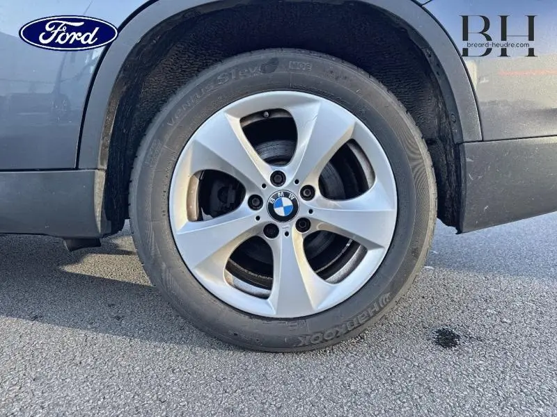 Gros plan sur la roue avant droite avec jante alu 17 pouces et logo BMW d’un BMW X1 Mineralgrau de 2013.