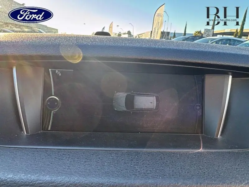 Écran multifonction intérieur montrant une vue aérienne du BMW X1 Mineralgrau en stationnement, avec reflets lumineux.