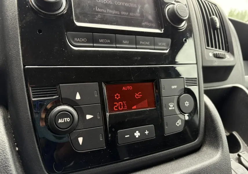 Vue rapprochée du tableau de bord noir de l'Opel Movano Fourgon 2023, mettant en valeur la climatisation automatique réglée à 20°C.