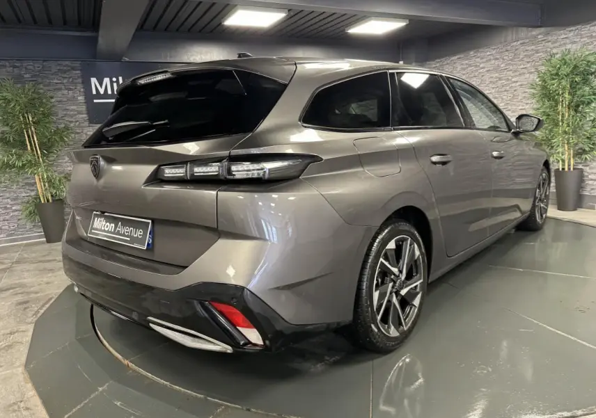 Vue 3/4 arrière droit d'une Peugeot 308 SW gris métallisé avec jantes alliage et feux arrière LED dans un showroom.