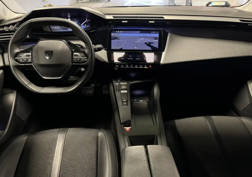 Intérieur avant de la Peugeot 308 SW 2022, tableau de bord noir avec écran tactile central et volant cuir compact.