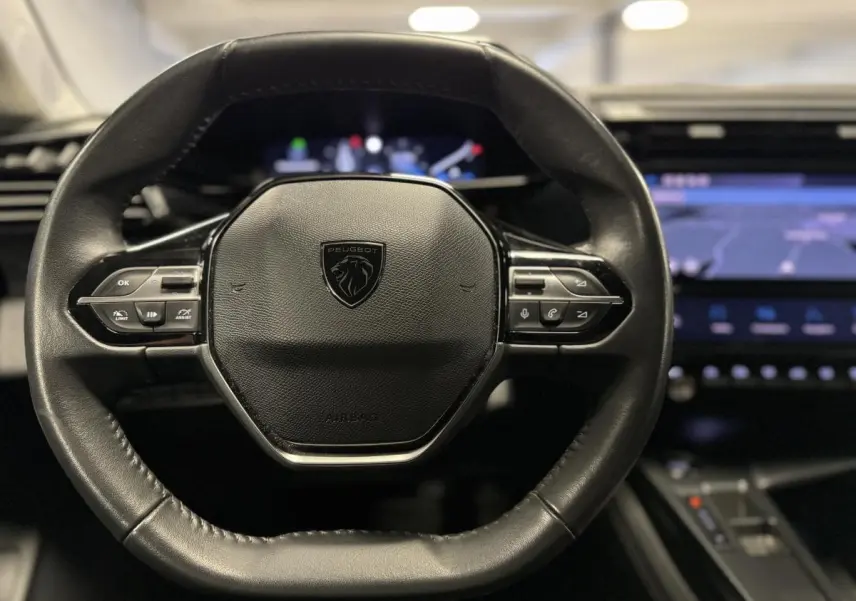 Volant cuir noir Peugeot 308 SW 2022 vu de face avec tableau de bord numérique et écran tactile bleu en arrière-plan.