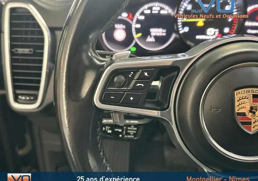 Gros plan sur le volant sport noir de la Porsche Cayenne E-Hybrid 2018 avec commandes intégrées et tableau de bord lumineux.