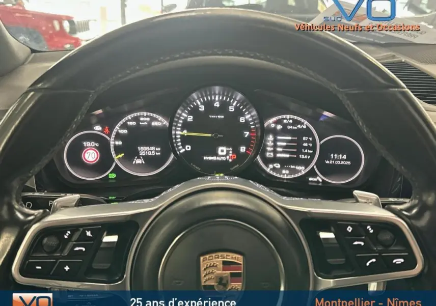 Vue rapprochée du tableau de bord et volant sport noir du Porsche Cayenne E-Hybrid 2018 avec compte-tours central.