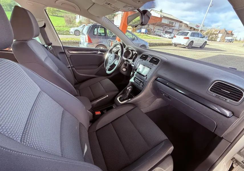 Intérieur avant d'une Volkswagen Golf blanche 2012, sièges tissu gris noir et tableau de bord avec écran tactile central.