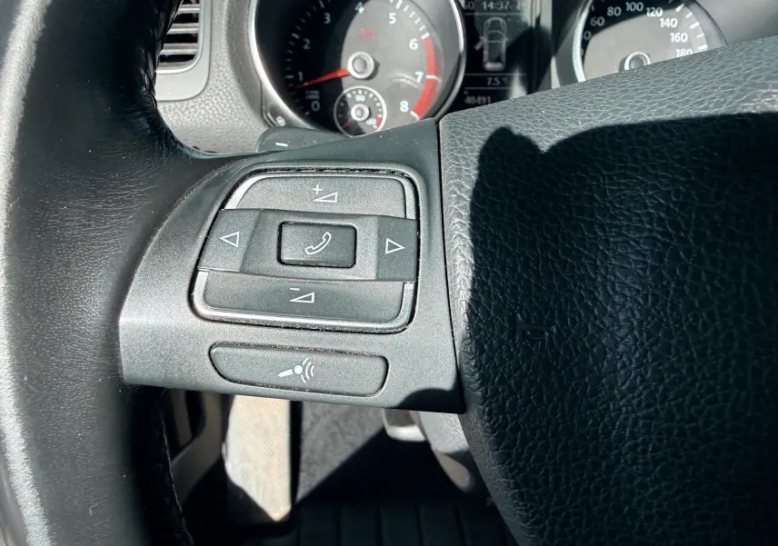 Gros plan sur les commandes du volant à gauche d'une Volkswagen Golf blanche, avec tableau de bord en arrière-plan.