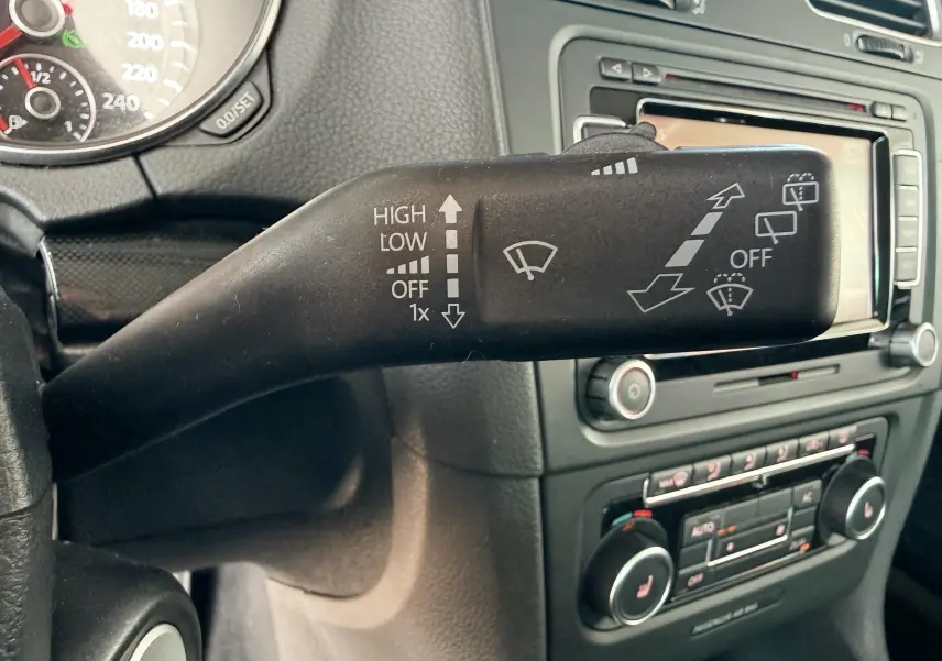 Gros plan sur la manette d'essuie-glace à gauche du volant dans l'habitacle gris noir d'une Volkswagen Golf blanche 2012.