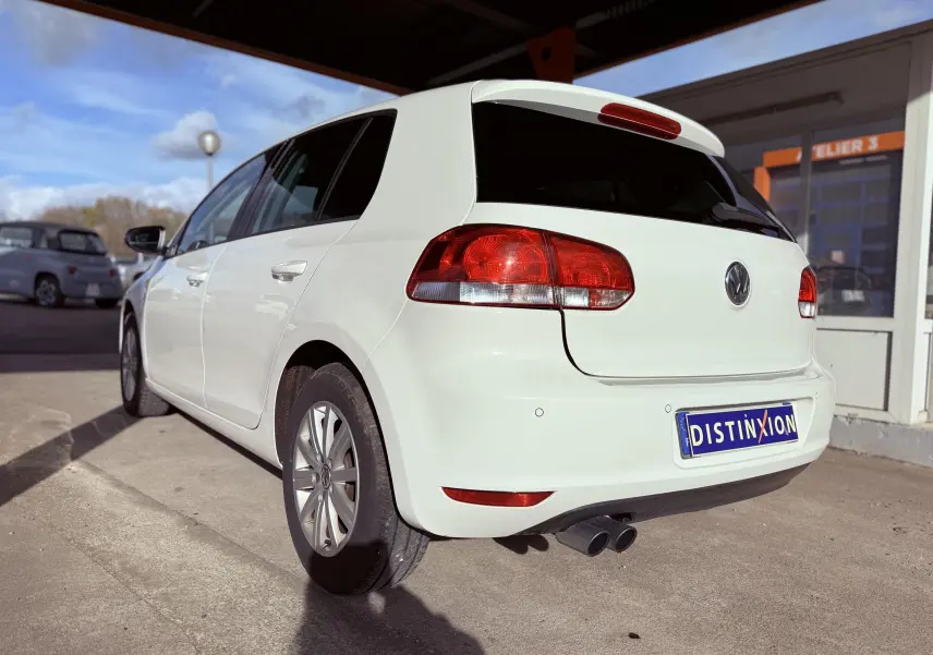 Volkswagen Golf blanc vue 3/4 arrière droit, avec feux rouges et double sortie d'échappement visible.