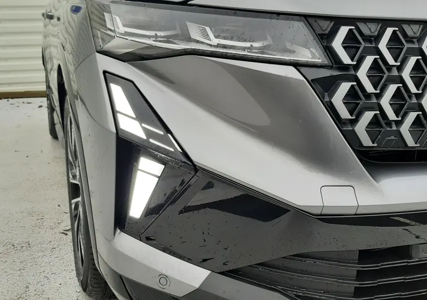 Gros plan 3/4 avant gauche du Renault Austral gris schiste avec phares LED et calandre hexagonale distinctive.