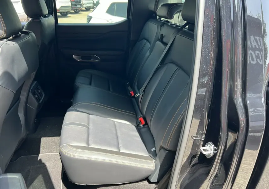 Vue intérieure côté arrière droit du Ford Ranger 2.3 PHEV Wildtrak Plus noir agate, montrant les sièges en cuir avec surpiqûres contrastantes.