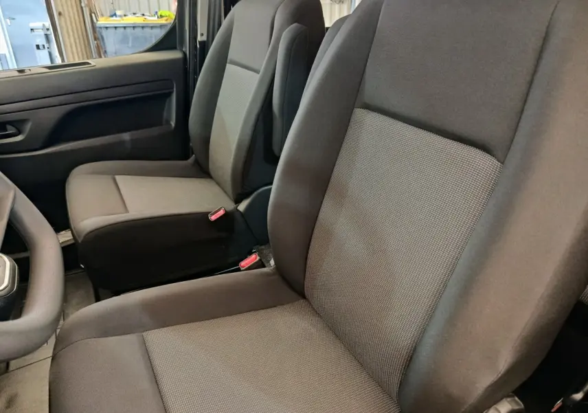 Vue intérieure côté conducteur du Citroën Jumpy gris foncé, montrant les sièges avant en tissu noir et gris.
