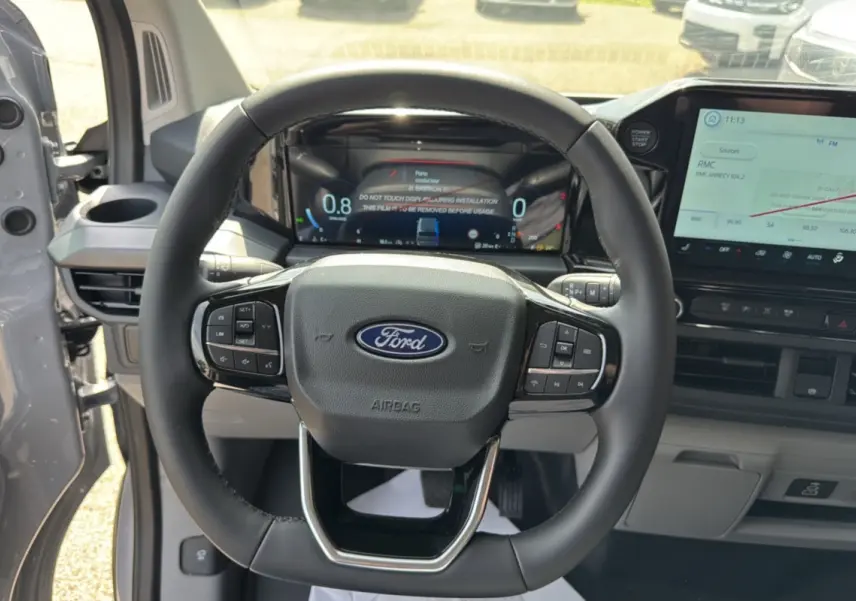 Vue intérieure centrée sur le volant multifonctions noir du Ford Transit Custom 2026, avec tableau de bord numérique et écran tactile.