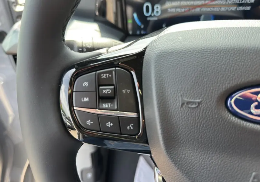 Gros plan sur le volant multifonctions gris du Ford Transit Fourgon Custom 170 BVA8 Sport 2026 avec commandes intégrées.
