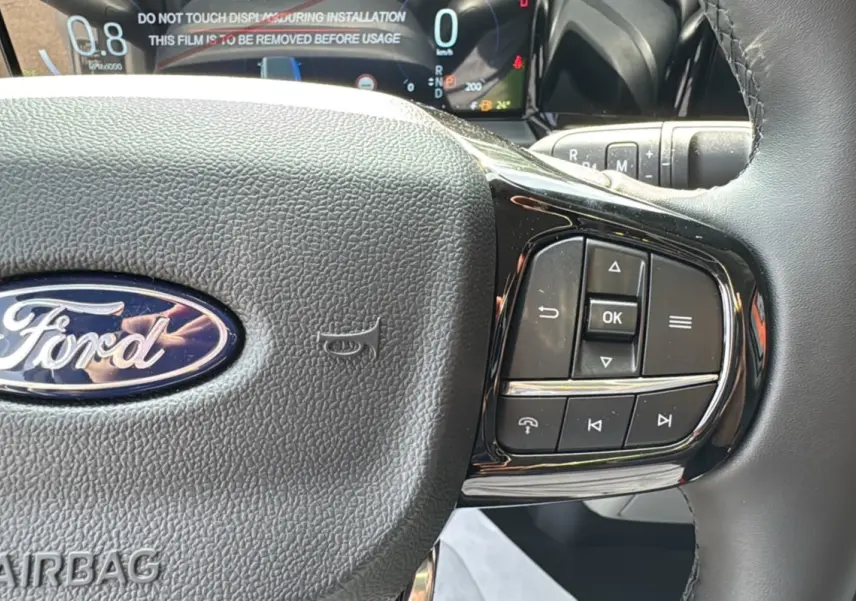 Gros plan sur le volant noir du Ford Transit Fourgon Custom 2026 avec commandes multifonctions et tableau de bord numérique.