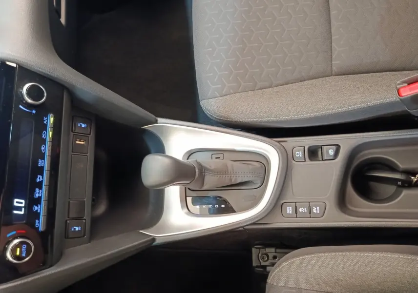Vue plongeante sur la console centrale grise avec levier de vitesse automatique et sièges tissu gris du Toyota Yaris Cross blanc.