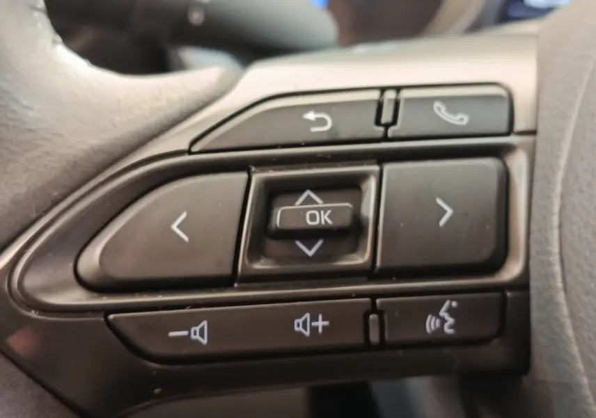 Gros plan sur les commandes multifonctions noires du volant de la Toyota Yaris Cross hybride blanche, version 2022.