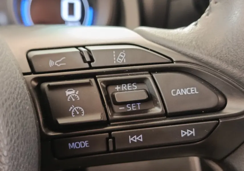 Gros plan sur les commandes au volant du Toyota Yaris Cross 1.5 Hybrid blanc, avec régulateur adaptatif et aide au maintien de voie.