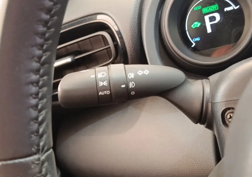 Gros plan sur la manette de commande des phares et clignotants côté gauche du tableau de bord noir d'une Toyota Yaris Cross hybride.