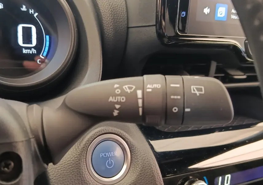 Gros plan sur le bouton démarrage bleu POWER et la commande d’essuie-glace dans l’habitacle noir de la Toyota Yaris Cross.