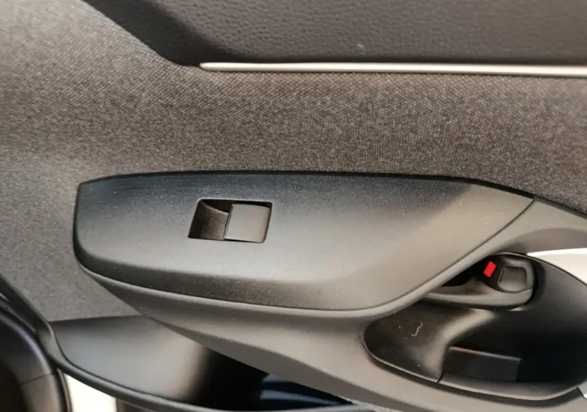Détail de la commande de lève-vitre côté conducteur noir dans l'habitacle de la Toyota Yaris Cross blanche.