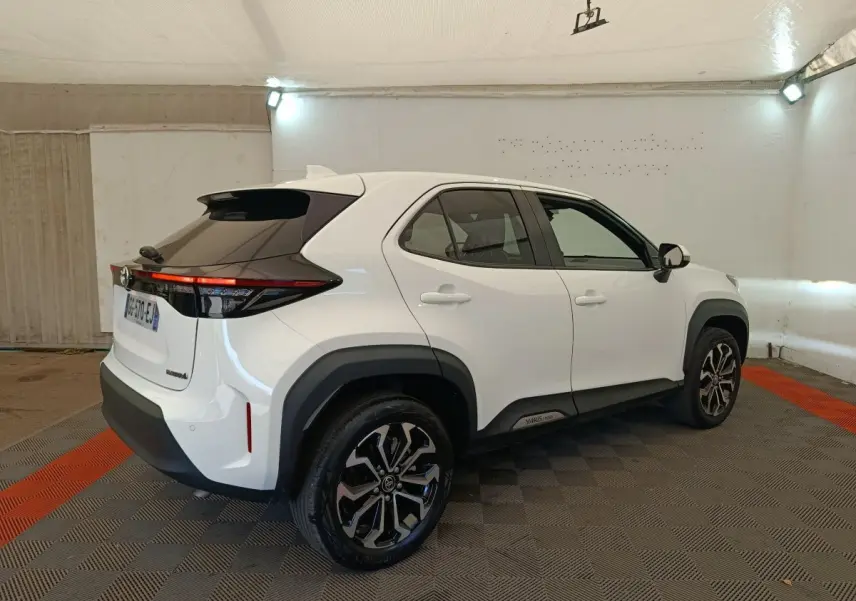 Vue 3/4 arrière droite d'une Toyota Yaris Cross blanche avec toit noir et jantes alliage bicolores dans un garage.