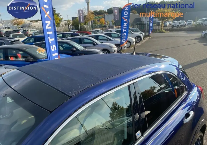 Vue latérale droite d'une FIAT 500X bleu Venezia Metal avec toit ouvrant en toile foncée, en extérieur sur parking.