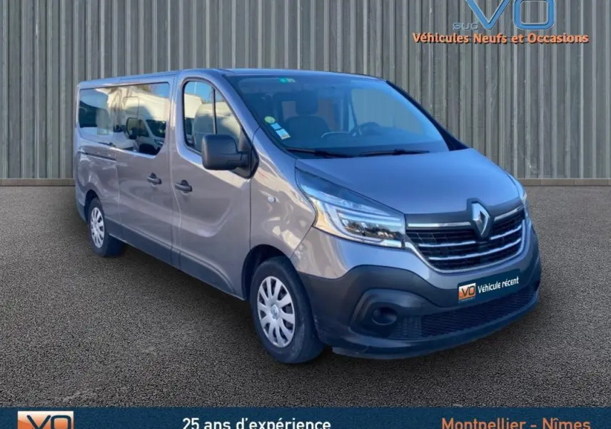 Renault Trafic Fourgon Combi gris clair vu en 3/4 avant droit avec porte latérale et vitres surteintées.