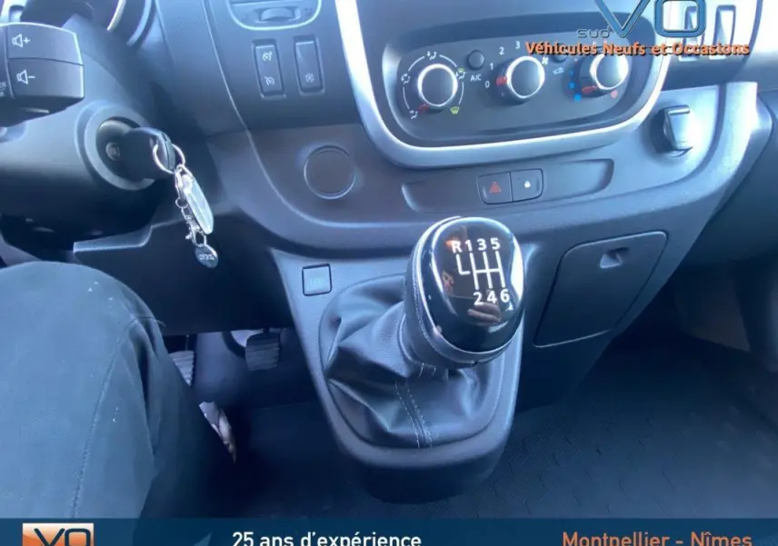 Gros plan sur le levier de vitesses manuel et le tableau de bord du Renault Trafic Fourgon gris clair de 2019.
