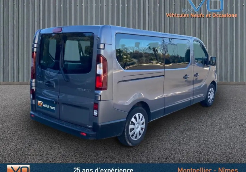 Vue 3/4 arrière droite d'un Renault Trafic Fourgon Combi gris clair avec vitres surteintées et porte latérale visible.
