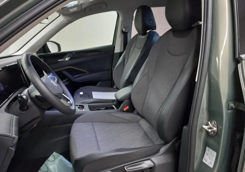 Vue intérieure côté conducteur du Volkswagen Tiguan 2025 vert Cipressino, sièges tissu noir et tableau de bord moderne.