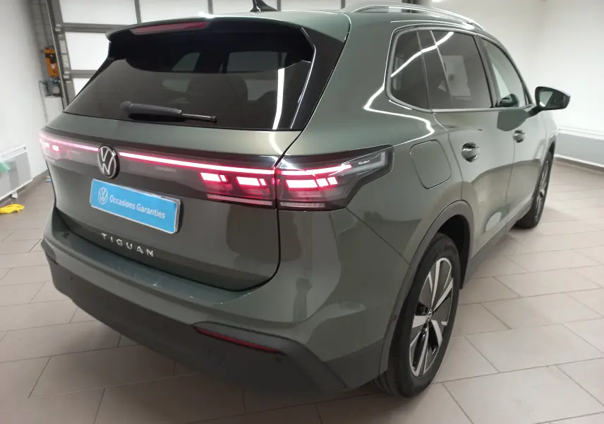 Volkswagen Tiguan 2025 Vert Cipressino, vue 3/4 arrière droit, feux arrière allumés et jantes alliage noir brillant.