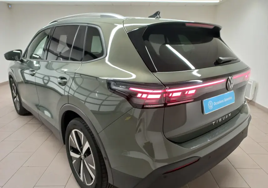 Vue 3/4 arrière gauche d'un Volkswagen Tiguan 2025 vert Cipressino avec jantes alliage noir brillant et feux arrière allumés.
