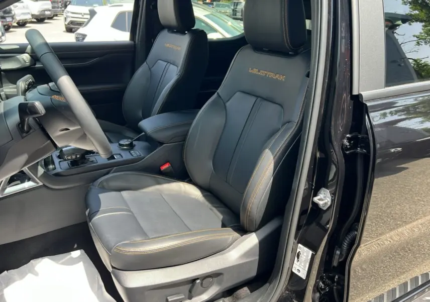 Vue intérieure côté conducteur du Ford Ranger Wildtrak 2.3 PHEV noir agate, sièges cuir avec surpiqûres orange et logo Wildtrak.