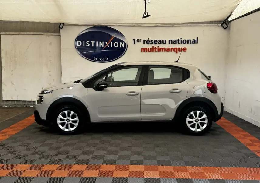 Profil droit d'une Citroën C3 beige 2021 dans un showroom, avec jantes alliage et protections noires sur les passages de roues.