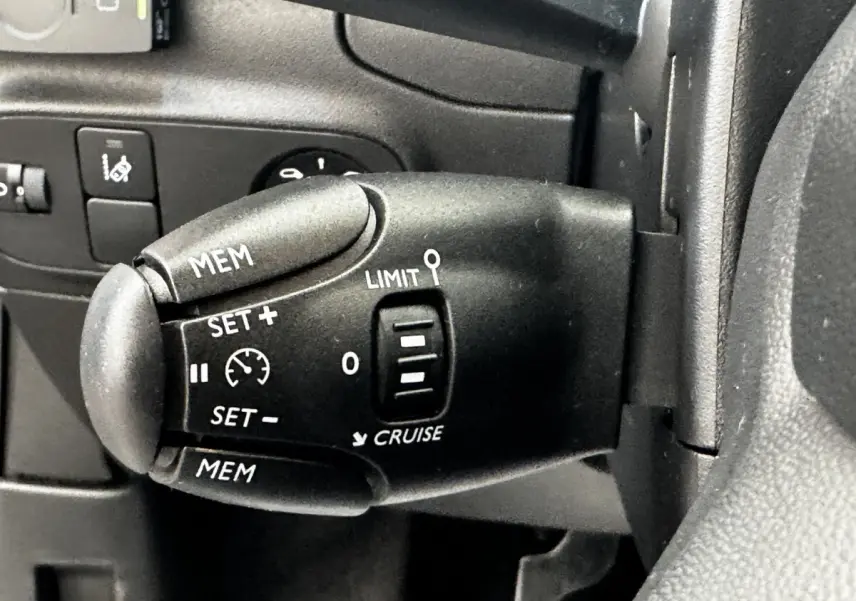 Gros plan sur la commande de régulateur de vitesse au volant d'une Citroën C3 beige, version PureTech 83 S&S BVM Feel.