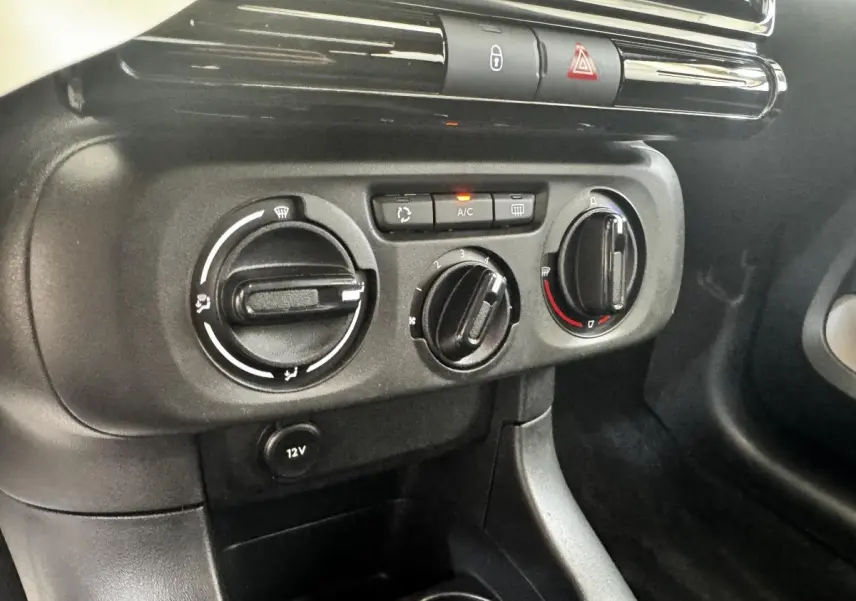 Gros plan sur les commandes de climatisation et prise 12V du tableau de bord intérieur de la Citroën C3 beige.