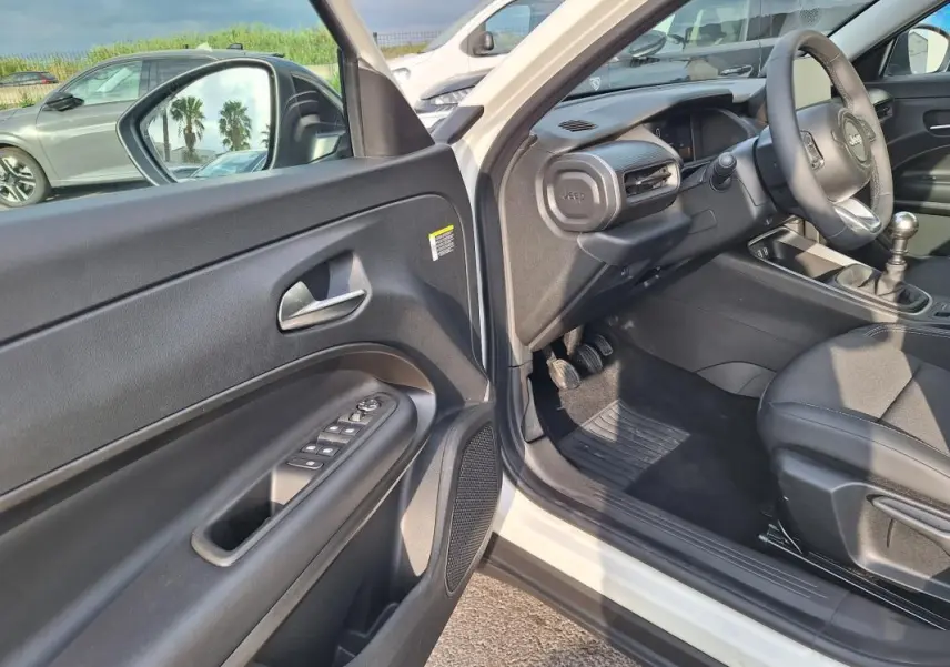 Vue intérieure côté conducteur du Jeep Avenger blanc 2025, montrant porte ouverte et tableau de bord noir.