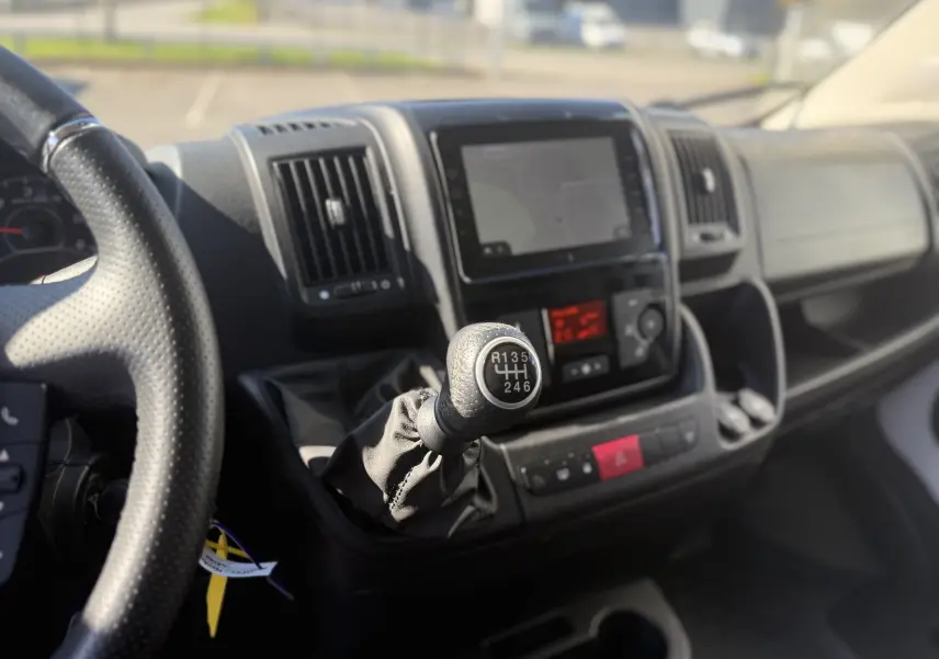 Vue intérieure centrée sur le levier de vitesses manuel noir du tableau de bord du fourgon Opel Movano blanc.