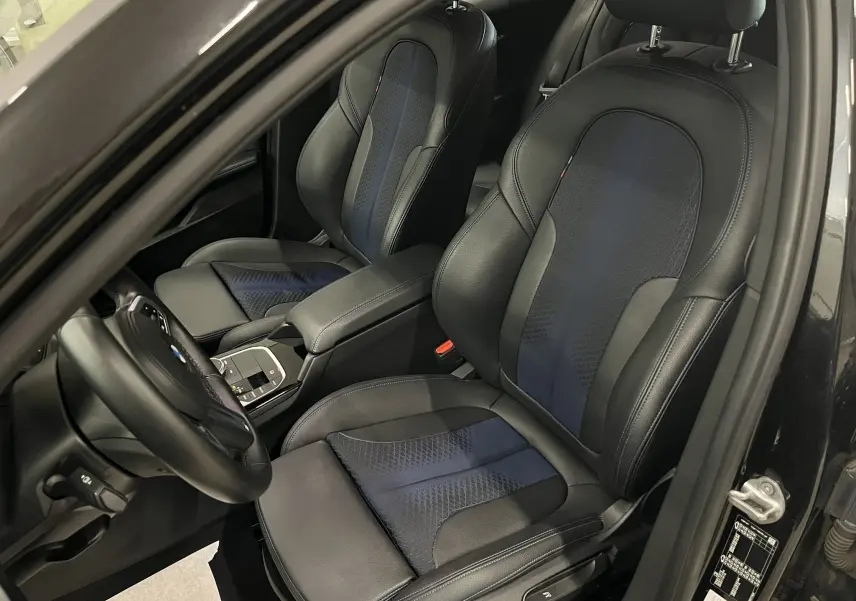 Vue intérieure côté conducteur de la BMW Série 1 F40 118dA 2020, sièges sport cuir noir avec inserts bleus et surpiqûres.