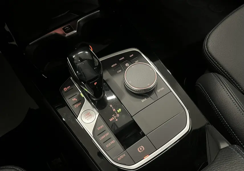Gros plan sur la console centrale noire brillante de la BMW Série 1 F40 118dA avec levier de vitesses et commandes de mode de conduite.