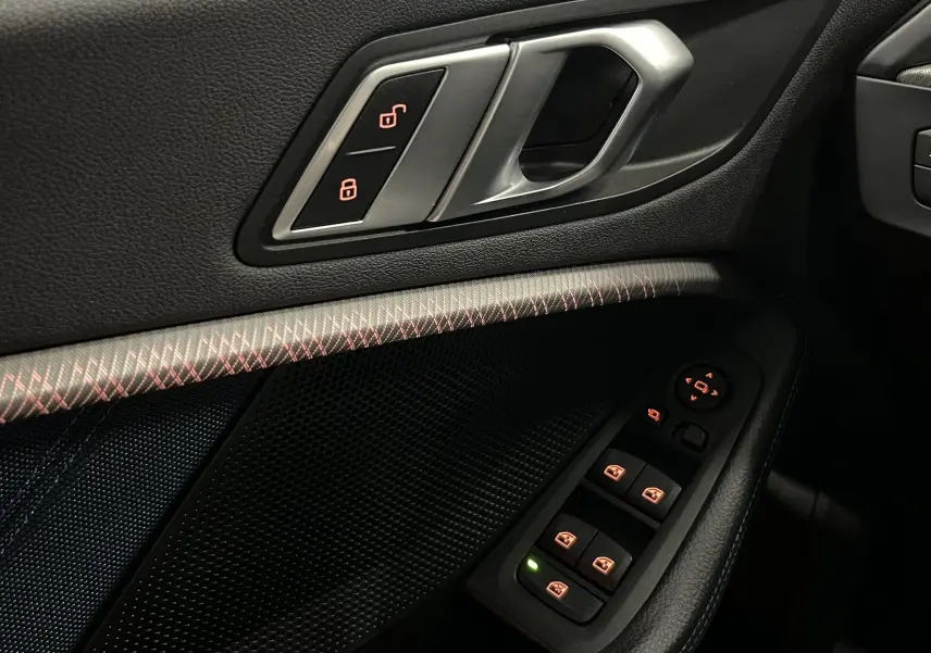 Gros plan sur la porte côté gauche de la BMW Série 1 F40 noire, montrant les commandes de verrouillage et les boutons de lève-vitres.