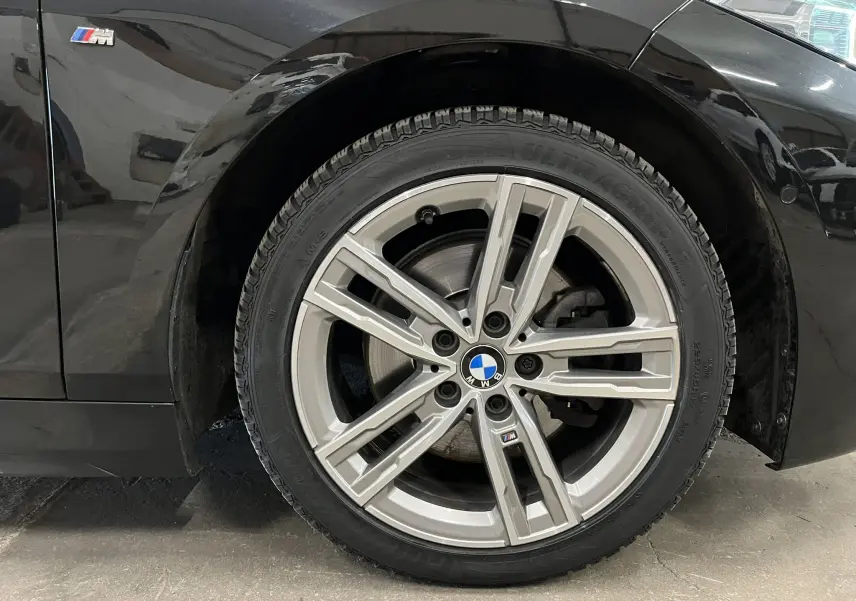 Gros plan sur la roue avant droite en alliage argenté avec logo BMW M sur une BMW Série 1 noire métallisée.