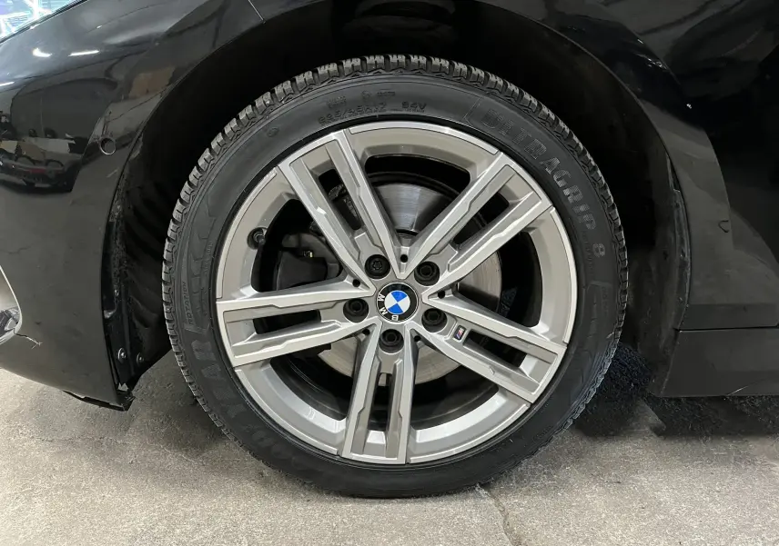 Gros plan sur la roue avant droite d’une BMW Série 1 noire métallisée avec jante alliage M sport à cinq branches doubles.