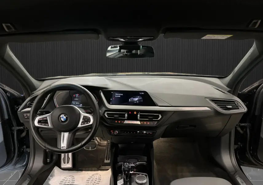 Vue intérieure avant de la BMW Série 1 noire, tableau de bord moderne avec écran central et volant sport M.