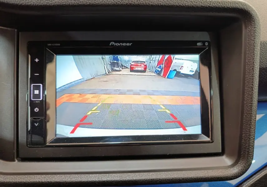 Écran de caméra de recul montrant l'arrière d'un véhicule blanc dans un garage, avec repères de guidage colorés.