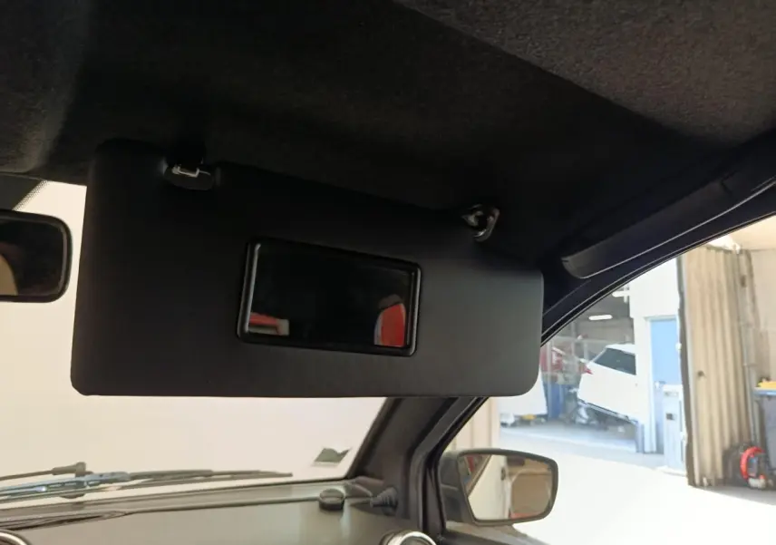Vue intérieure côté conducteur d'un Aixam Ambition blanc 2023, avec pare-soleil abaissé et rétroviseur extérieur visible.