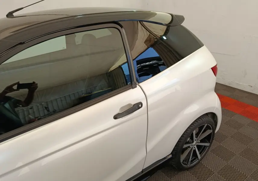 Vue côté gauche arrière d'une Aixam Ambition 0.5 City Coupe GTI blanche avec toit noir et jante alliage noire.