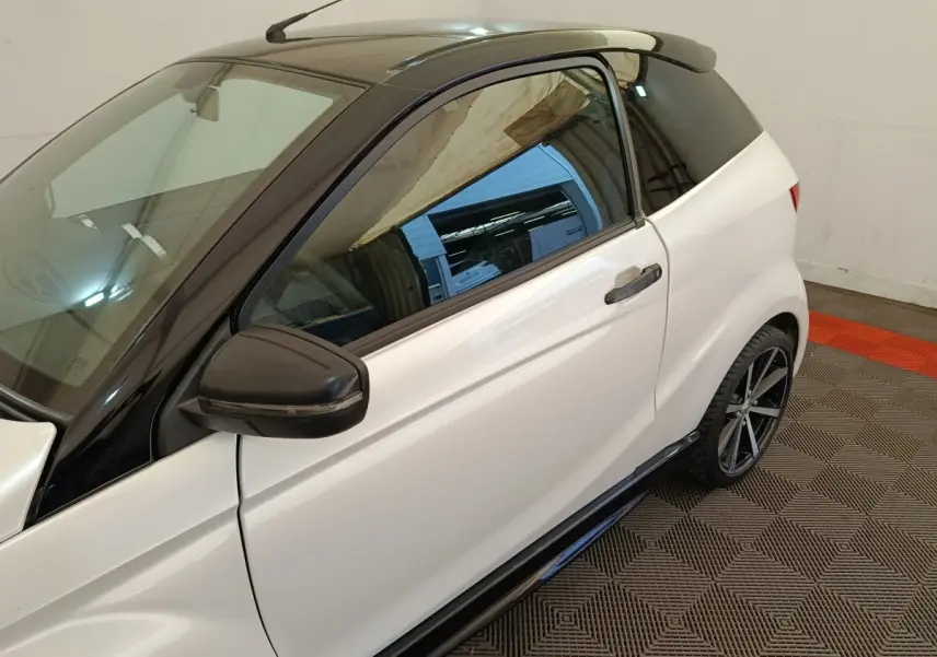 Vue côté gauche rapprochée de l'AIXAM AMBITION 0.5 CITY COUPE GTI blanche avec toit noir et rétroviseur conducteur noir.